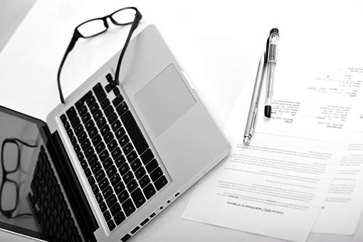 Laptop, papers, pen, and reading glasses on a desk