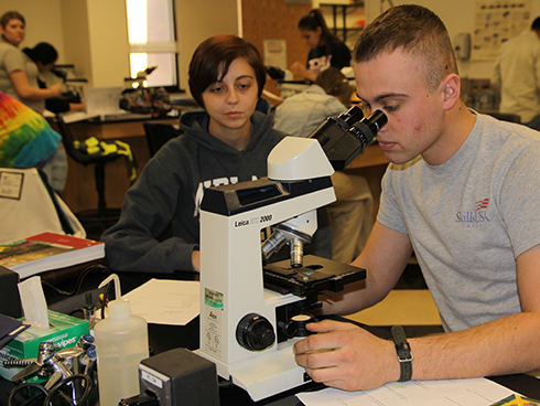 One student looks through a microscope while another watches